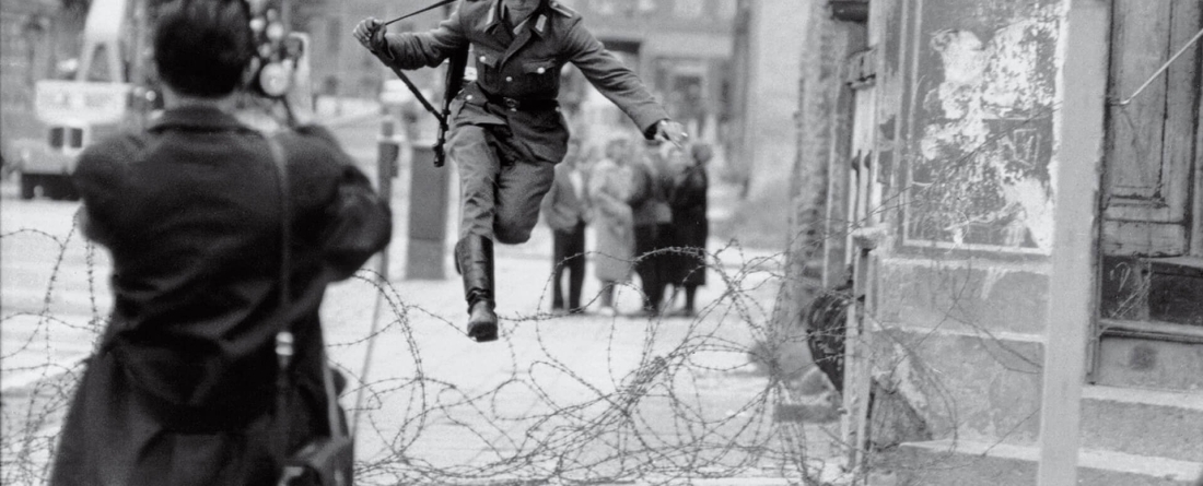 Photograper snapping photo of military man jumping over barbed wire