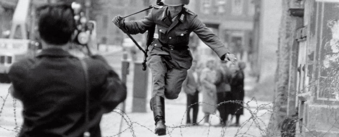 Photograper snapping photo of military man jumping over barbed wire